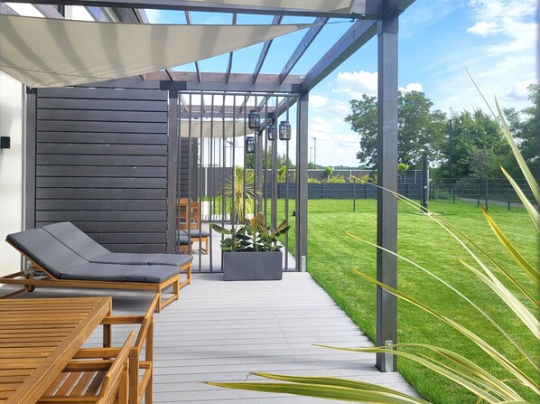 A covered patio with wooden furniture, a planter with plants, and a view of a well-maintained lawn.