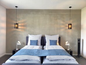 A double bed with a grey headboard, two bedside tables with lamps, and a large window with a view of the city skyline.