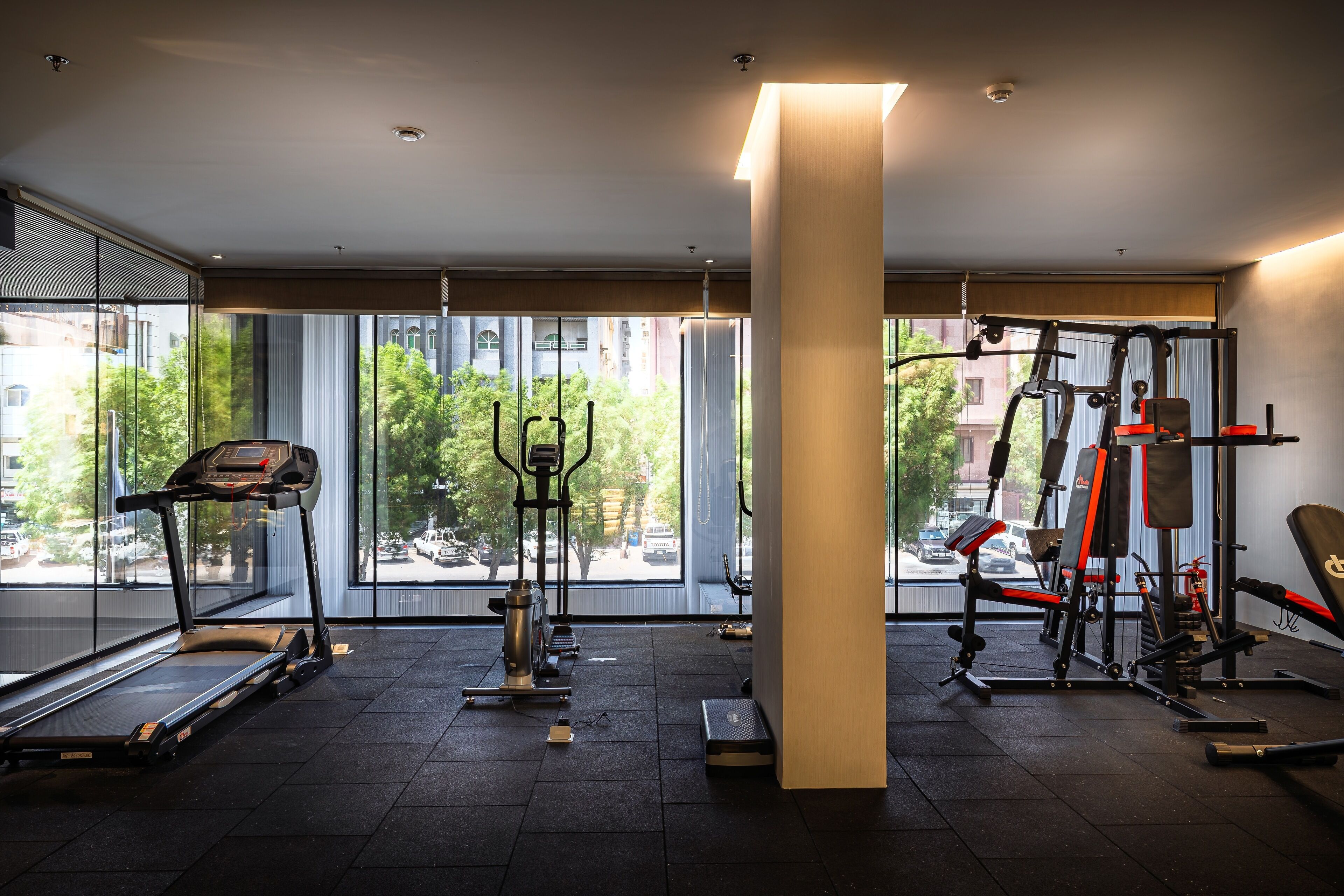 A modern gym with a treadmill, elliptical, and weight machines. Large windows offer views of the city.