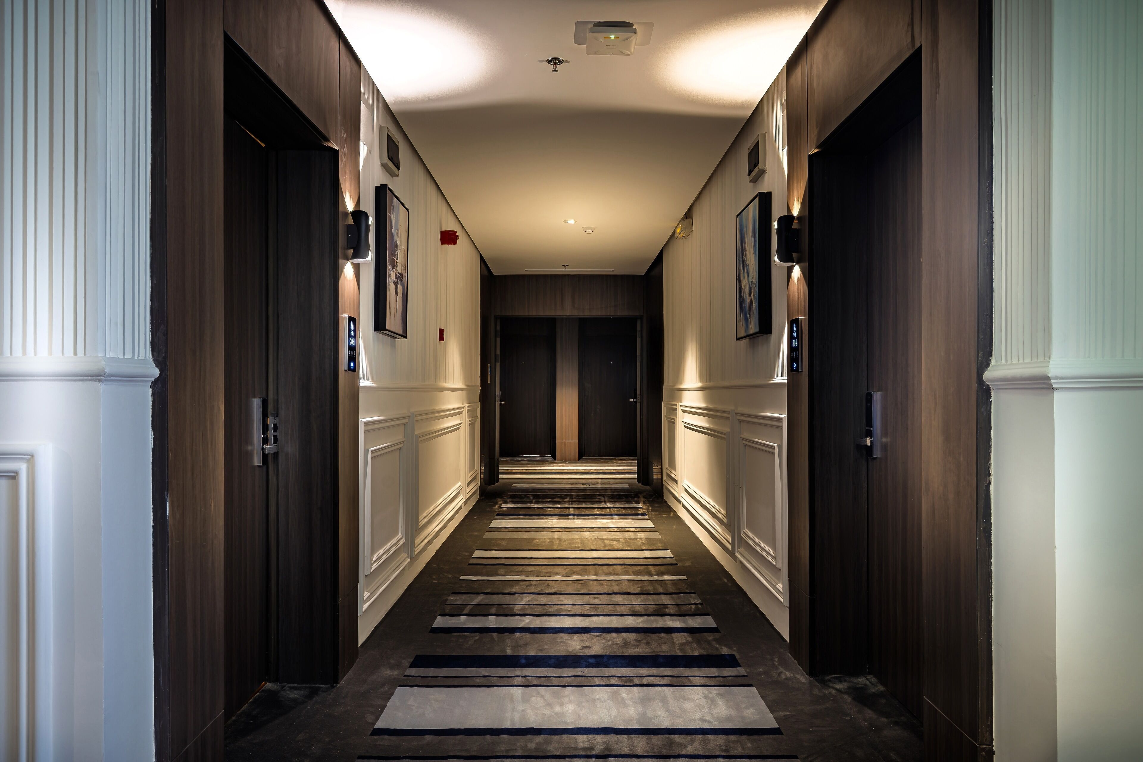 A hotel hallway with wooden doors, a carpeted floor, and a ceiling light fixture.