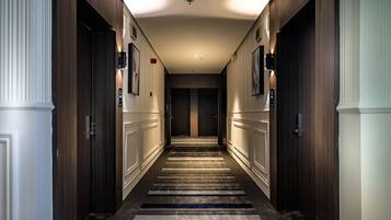 A hotel hallway with wooden doors, a carpeted floor, and a ceiling light fixture.