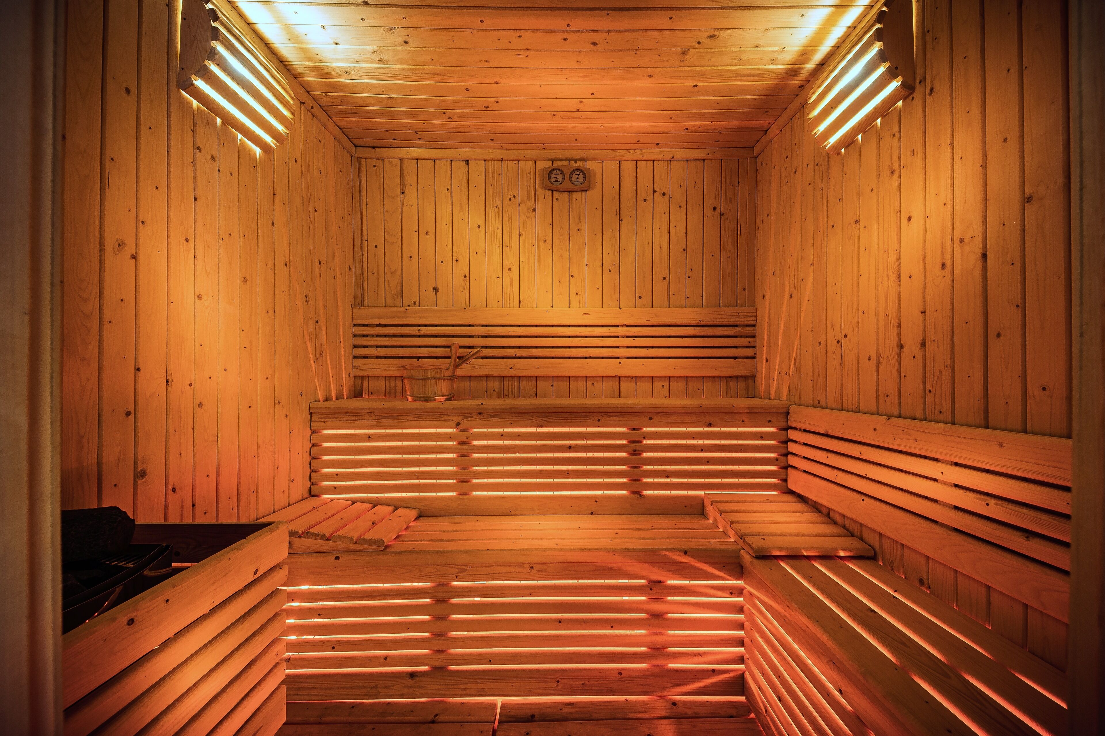 A sauna with wooden benches and slatted floors, illuminated by overhead lights.