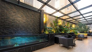 Un espacio interior moderno con techo de vidrio, pared de piedra y zona de piscina.