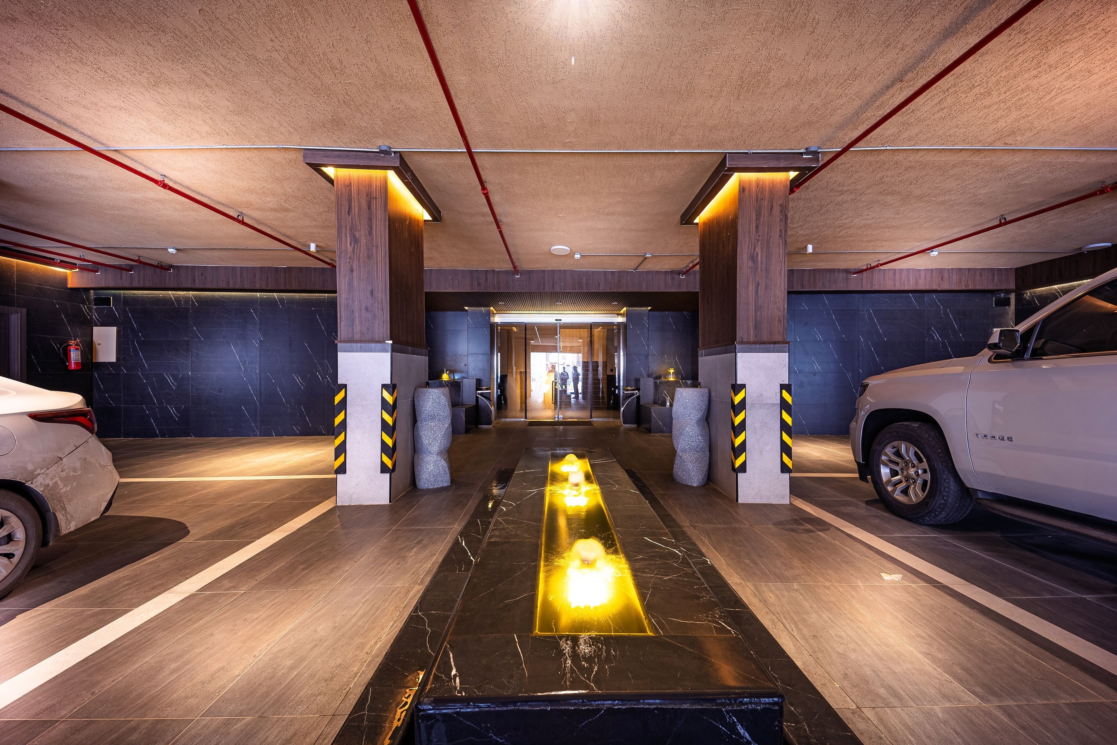 Un parking souterrain moderne, doté d’une allée centrale illuminée, de piliers en béton et de voitures garées de part et d’autre.