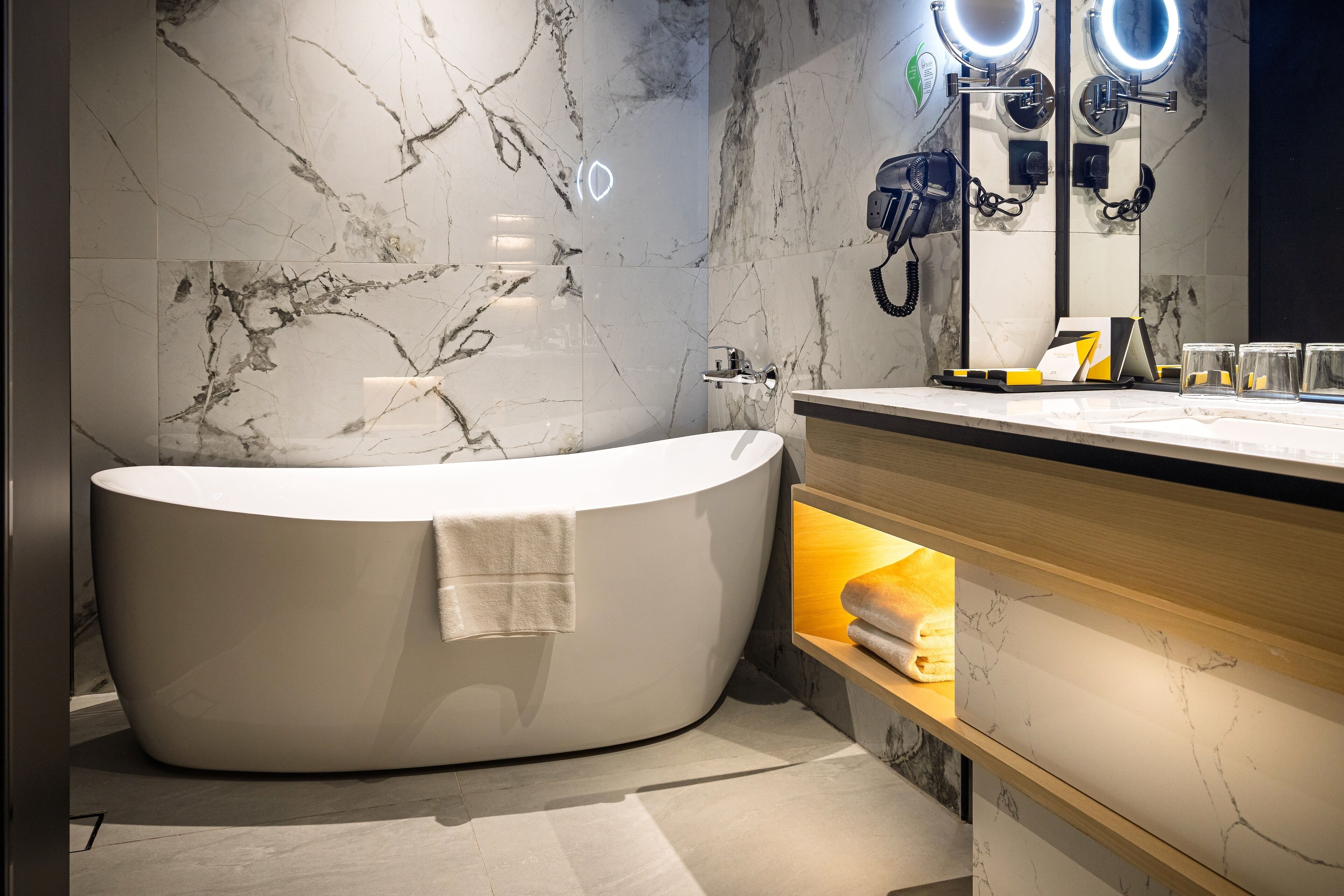 Un baño moderno con una bañera independiente, paredes de mármol y un tocador con espejo e iluminación.
