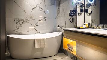 Un baño moderno con una bañera independiente, paredes de mármol y un tocador con espejo e iluminación.