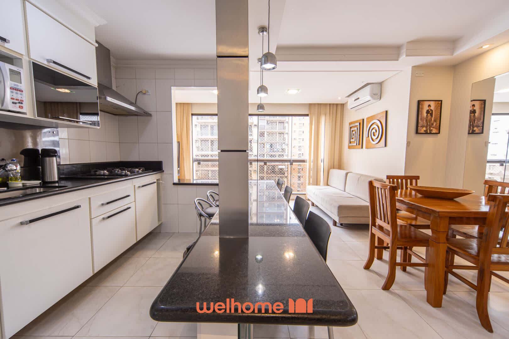 A modern kitchen with white cabinets, a black countertop, and a dining area with wooden furniture.