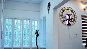 A room with a wooden floor, large windows, a wall-mounted tree decoration, and a wall-mounted light fixture. - Nature Harmony (Udumbanchola)