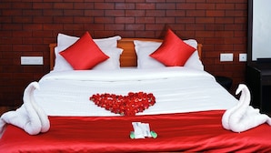A hotel room with a brick wall, a ceiling fan, a bed with red and white bedding, and a swan decoration. - Nature Harmony (Udumbanchola)
