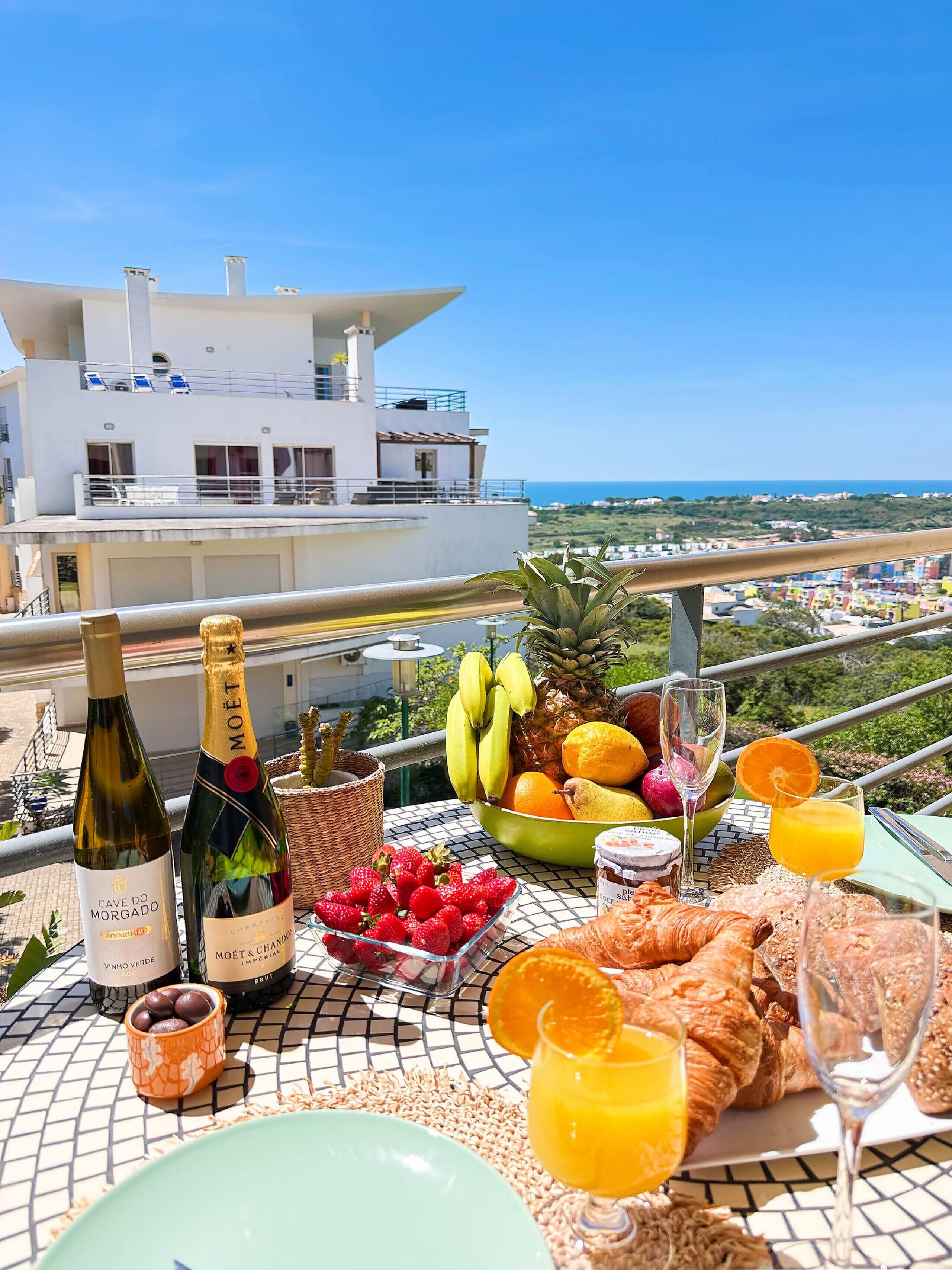 Ein Balkon mit Frühstückstisch, gedeckt mit Obst, Gebäck und Getränken, mit Blick auf die Küste.