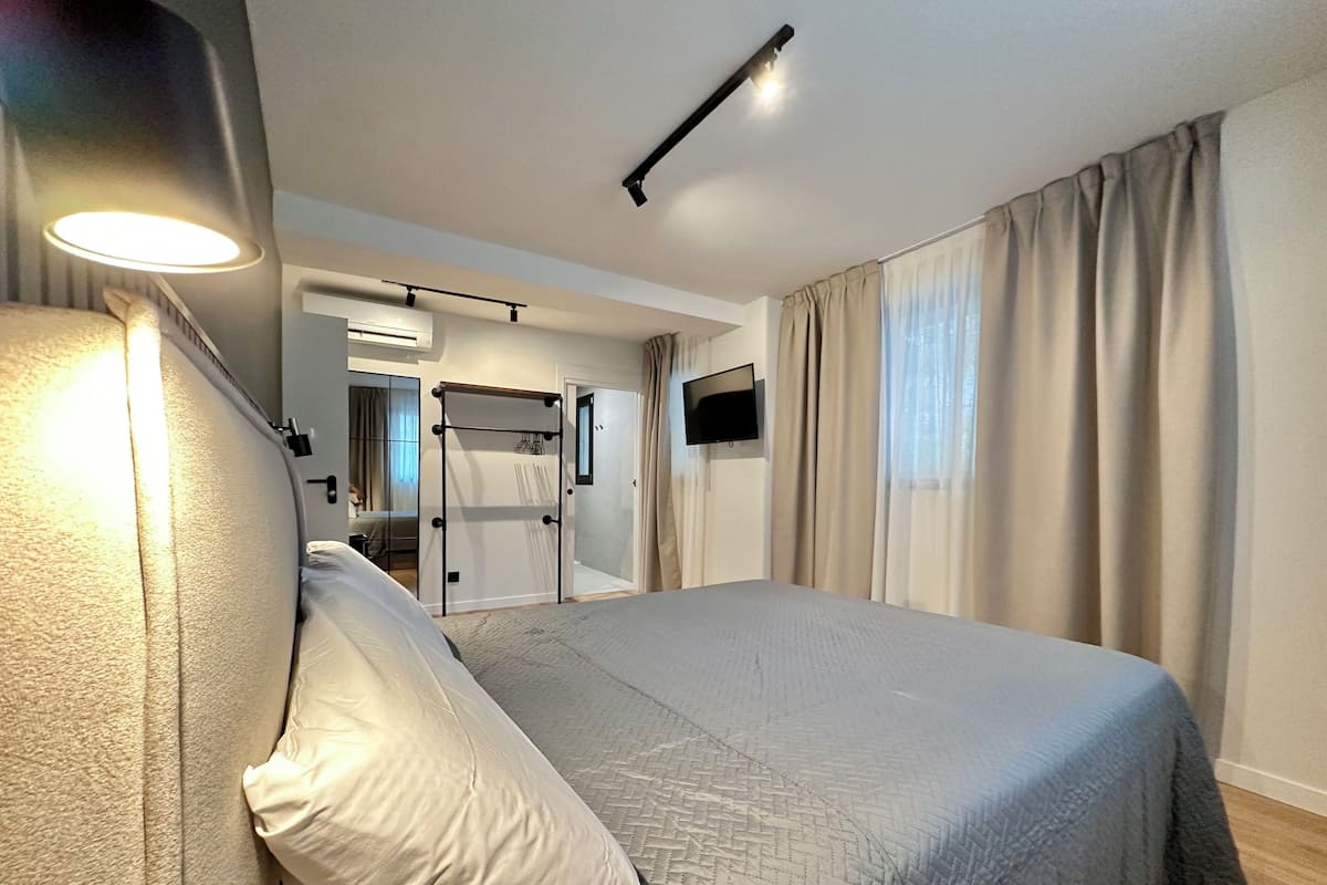 Ein modernes Hotelzimmer mit einem großen Bett, einem Nachttisch, einem an der Wand befestigten Fernseher und einem Fenster mit Vorhängen.