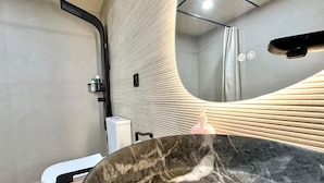 A modern bathroom with a large marble sink, a handheld showerhead, and a towel rack.