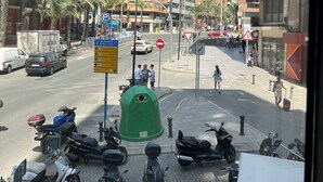 A busy urban street with parked scooters and a green trash bin.
