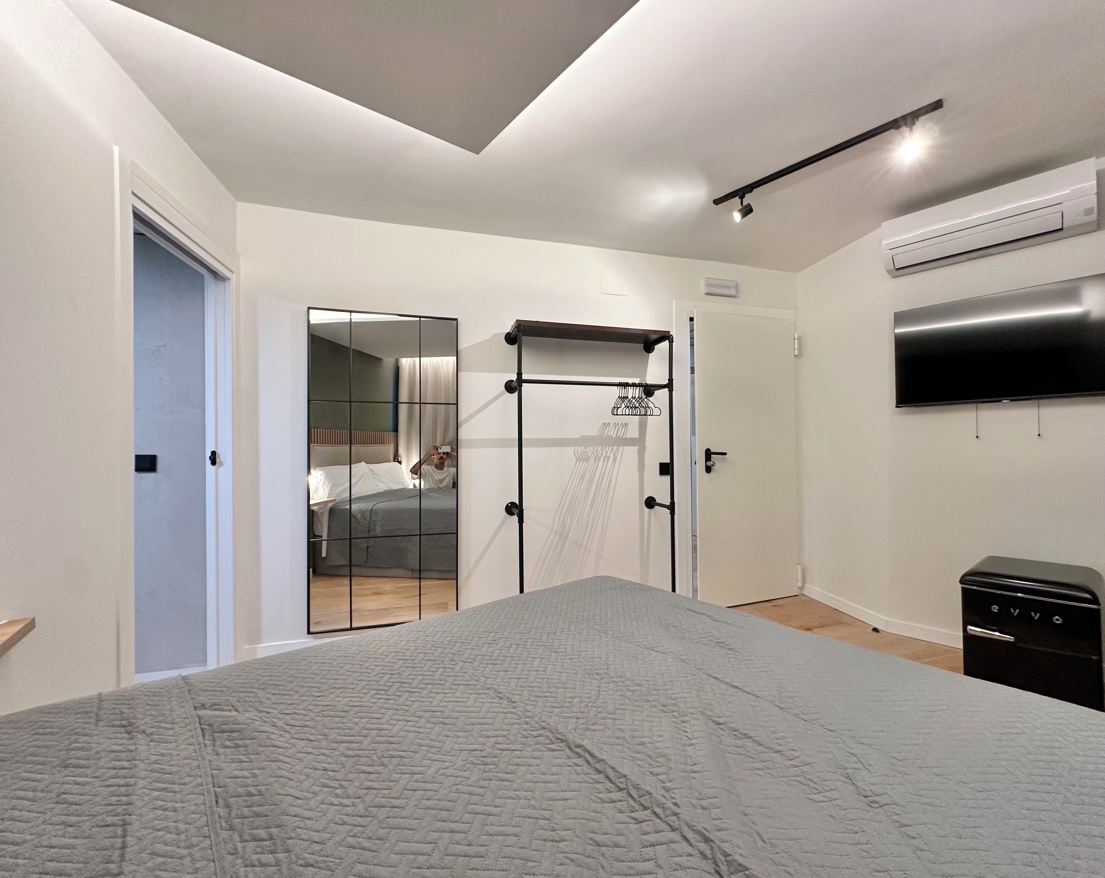 A modern bedroom with a large bed, a wardrobe, a mirror, and a TV.