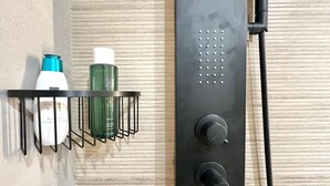 A bathroom with a black shower panel, a metal shelf holding toiletries, and a wooden wall.