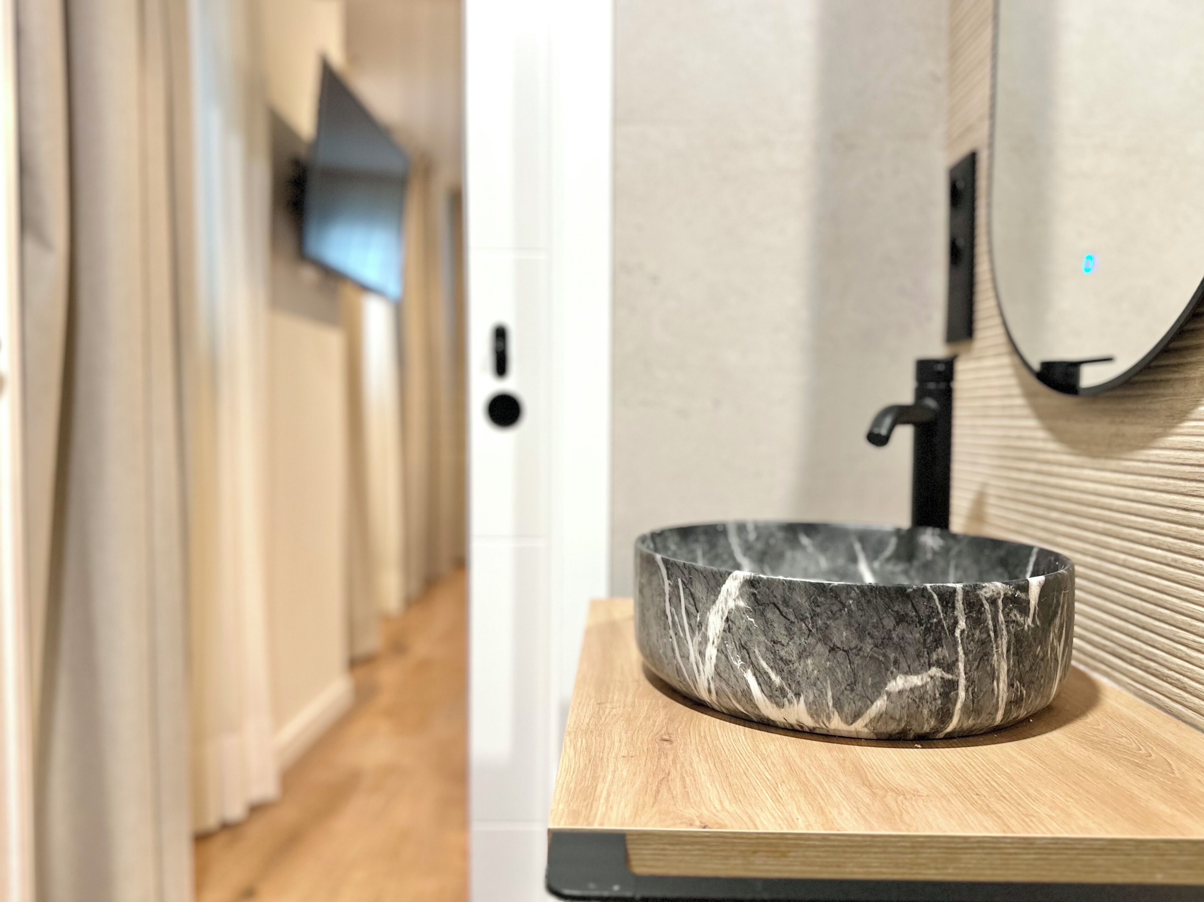Un baño moderno con lavamanos de mármol, encimera de madera y un perchero para toallas.