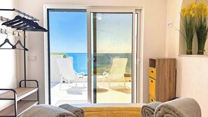 Una habitación con cama, una silla, una mesa, un armario y vista al mar a través de un ventanal corredero.