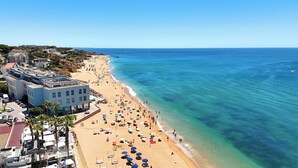 Un hotel frente a la playa con varios pisos, una playa de arena y aguas azules cristalinas.