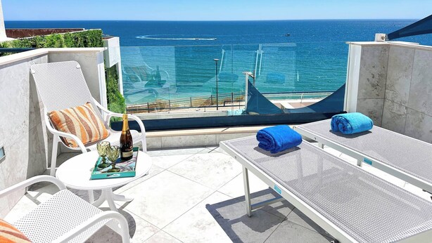 Una terraza con vistas al mar, con dos sillones de relax, una mesa con una botella y una revista, y una toalla azul.