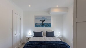 Ein Schlafzimmer mit einem Bett, zwei Nachttischen, einem Wandbild eines Walrückens und einer Tür.