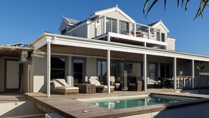 Ein zweistöckiges Haus mit Pool, Sitzgelegenheiten im Freien und einer überdachten Terrasse.