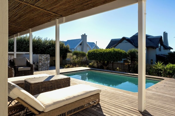 Un espace piscine avec des chaises longues, une terrasse en bois et une vue sur les maisons au loin.