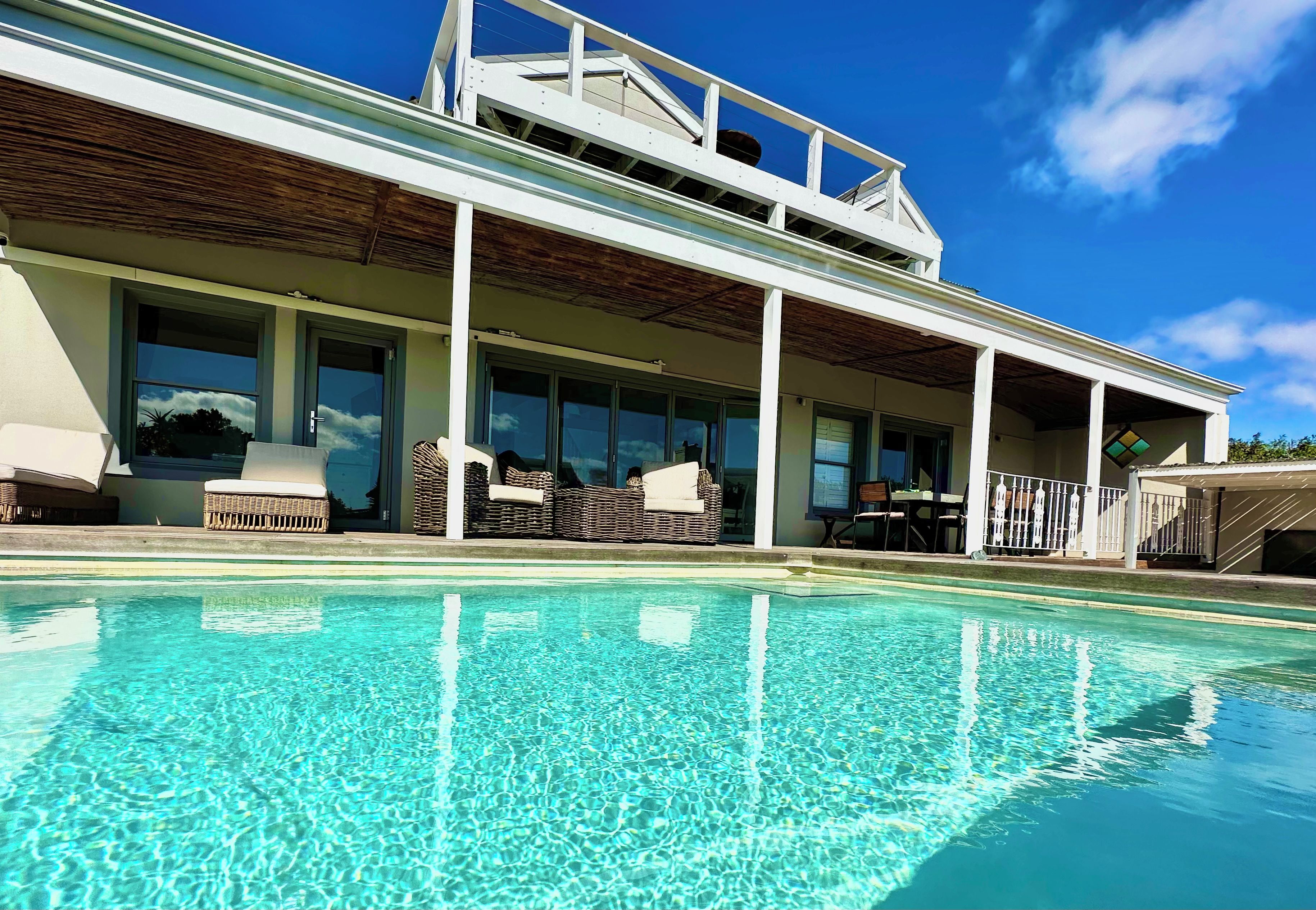 Une maison moderne dotée d’une piscine, de grandes fenêtres et de mobilier d’extérieur.