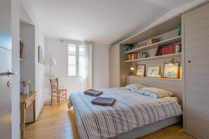Un dormitorio con una cama, una silla, un escritorio, una estantería y una ventana.