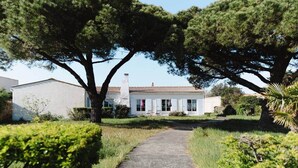 A white building with a tiled roof, a paved pathway leading to the entrance, and surrounding greenery. - Villa Kenavo - Family house with sea view (Île-d'Aix)
