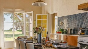 An open-plan kitchen and dining area with a view of the outdoors, a tiled backsplash, and a wooden dining table set for a meal. - Villa Kenavo - Family house with sea view (Île-d'Aix)
