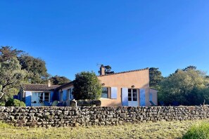 A two-story house with a stone wall in front, a tiled roof, and a chimney.