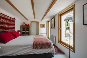 A bedroom with a bed, a red throw blanket, a wooden cabinet, and a window with a view of the outdoors.