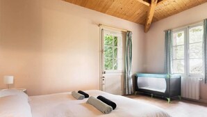 A bedroom with a large bed, a window with curtains, a radiator, and a small table with a play mat. - Marais Aixois-Villa-Villa-Ensuite Bathroom-View of the (Île-d'Aix)
