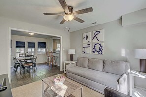 A living room with a sofa, coffee table, and a ceiling fan. There is a dining area with a table and chairs.