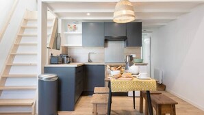 A compact kitchen with a built-in island, wooden flooring, and a hanging light fixture. - La Miniardise - House in the village (Île-d'Aix)