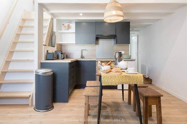 A compact kitchen with a built-in island, wooden flooring, and a hanging light fixture.