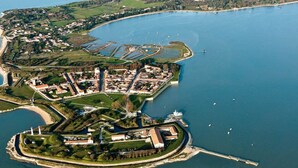 An aerial view of a coastal town with a fortified structure, a marina with boats, and a lighthouse. - La Miniardise - House in the village (Île-d'Aix)