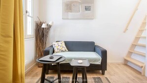 A small living area with a sofa, two small tables, a lamp, and a painting on the wall. - La Miniardise - House in the village (Île-d'Aix)
