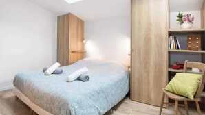 A bedroom with a bed, a wooden wardrobe, a skylight, and a small desk with a chair. - La Miniardise - House in the village (Île-d'Aix)