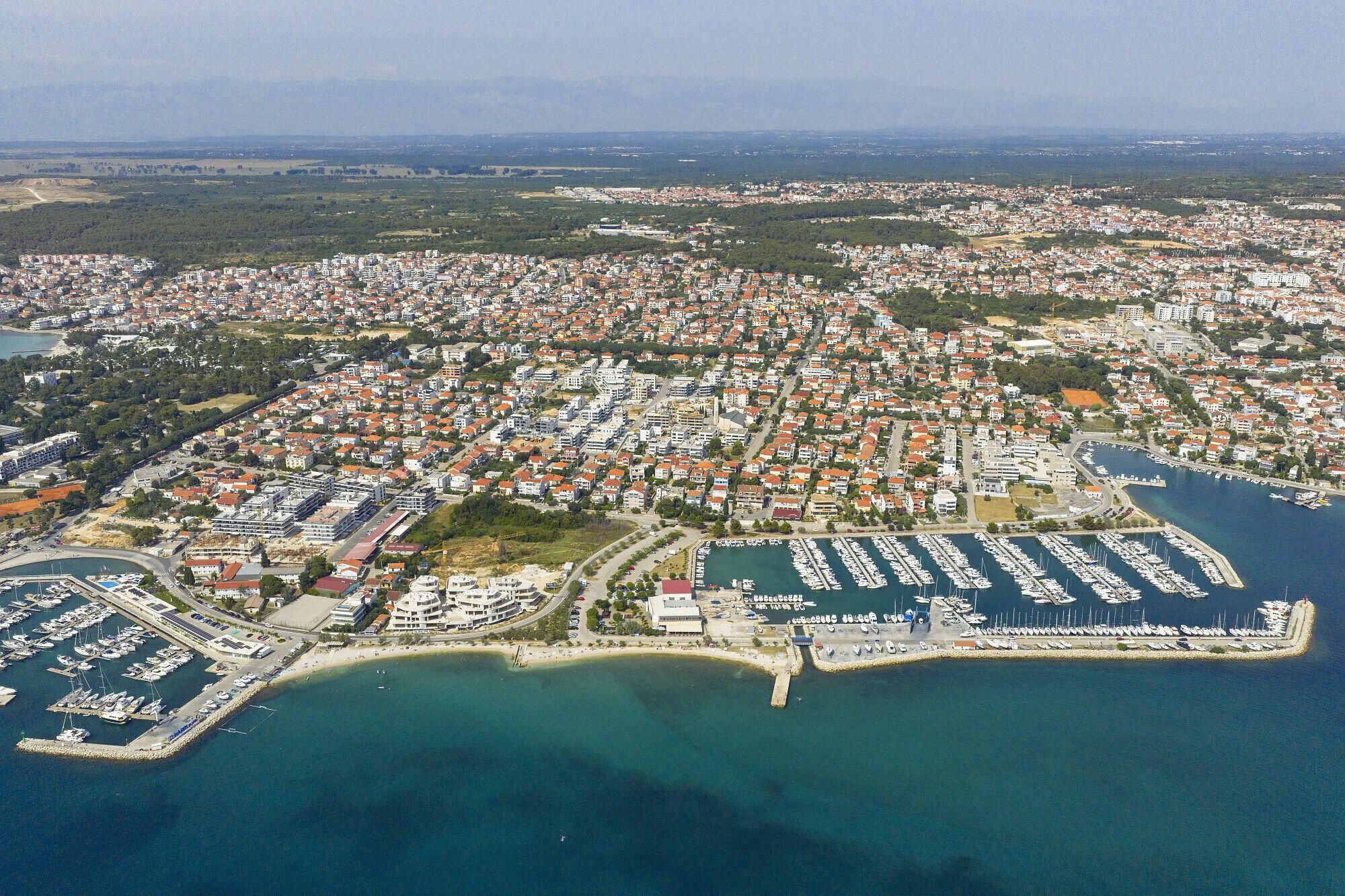 Vue aérienne d’une ville côtière avec des quartiers résidentiels, un port de plaisance et une plage.