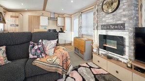 A cozy living area with a sofa, a fireplace, and a kitchen in the background. - Host & Stay | Leon's Retreat (Cresswell)