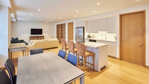 A modern kitchen with a central island, a dining area with a table and chairs, and a living area with a sofa and TV. - Host & Stay | Thames Apartment (Windsor)