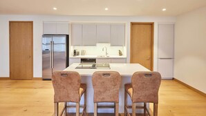 A modern kitchen with a central island, three bar stools, and a refrigerator. - Host & Stay | Thames Apartment (Windsor)