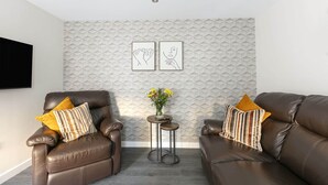 Ein modernes Wohnzimmer mit zwei Ledersofas, einem kleinen runden Tisch mit Blumenvase und zwei gerahmten Kunstwerken an der Wand.
