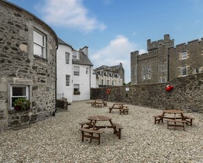 A courtyard with stone buildings, wooden picnic tables, and a gravel ground. - Kerrycroy Luxury Accessible Ground Floor Apartment~Pet Friendly~Private Parking (Rothesay)