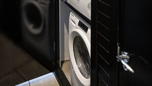A laundry room with a washing machine and dryer, a tiled floor, and a black door. - Scalpsie Luxury Apartment (Rothesay)