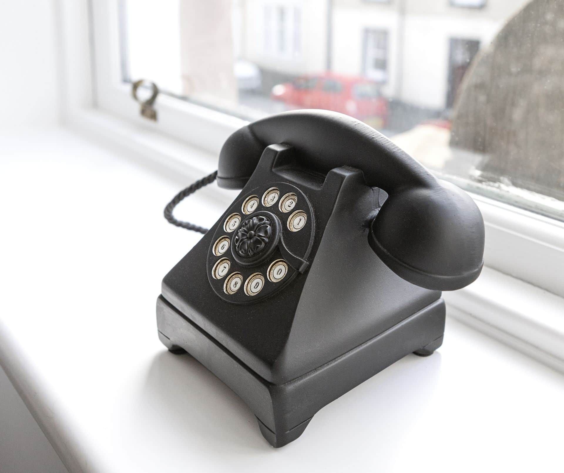 Un teléfono antiguo con dial giratorio negro sobre un alféizar.