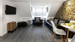 A modern loft-style living room with a black leather sofa, a white dining table, and a stone accent wall.