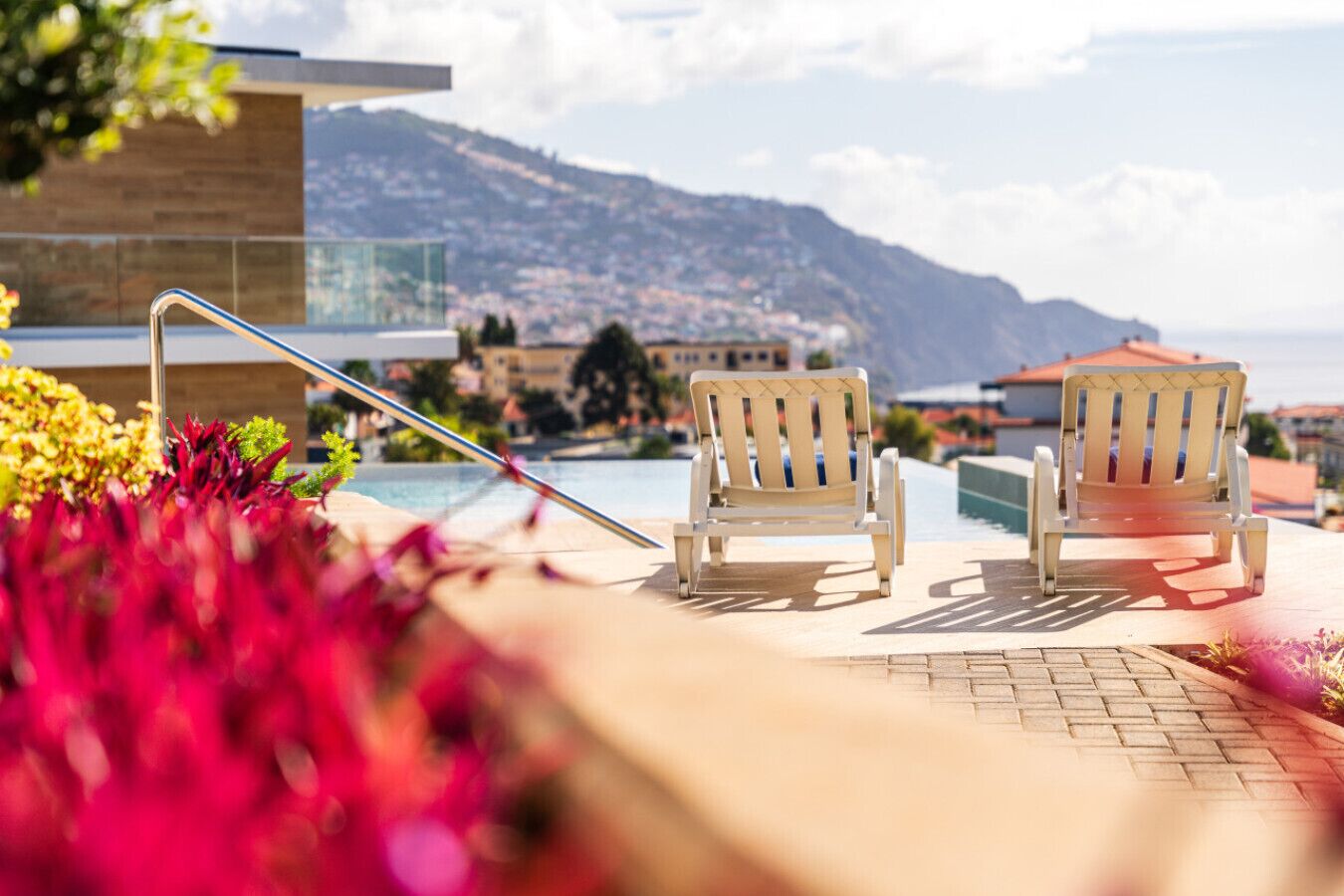 A poolside area with two lounge chairs and a poolside table, overlooking a mountainous landscape.