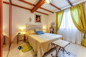 A bedroom with a bed, bedside tables, a nightstand, a lamp, a bedside shelf, a window with curtains, and a painting on the wall. - Apartment 'Gîte Le Séguret' with Mountain View and Wi-Fi (Entrechaux)